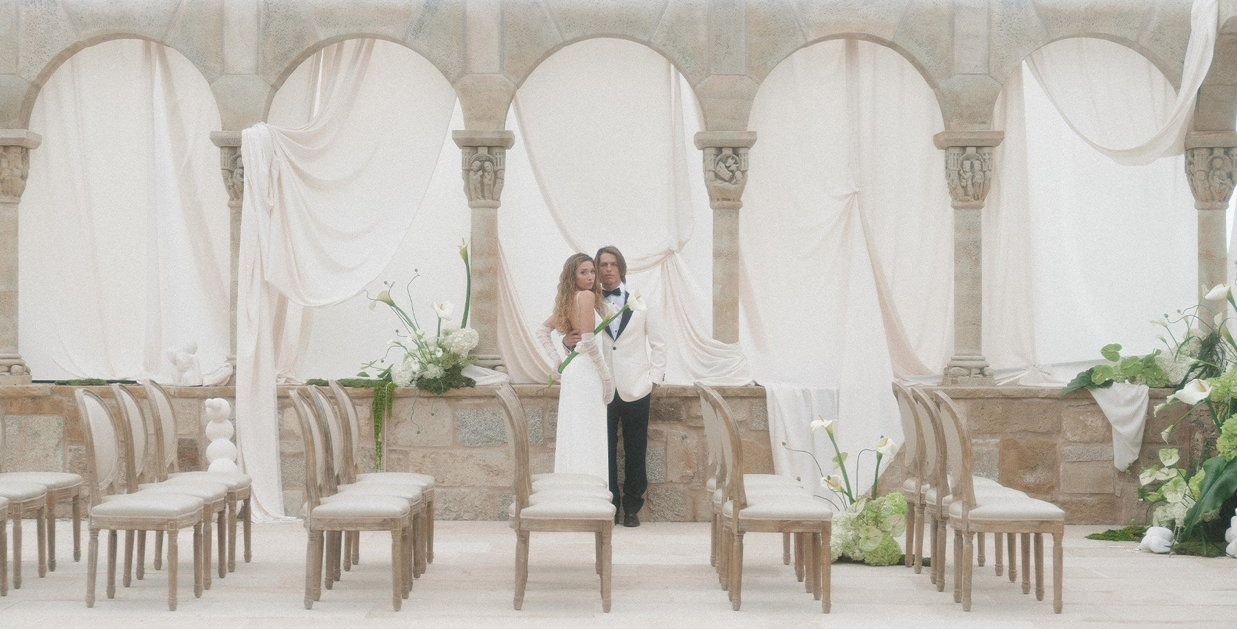 Minimalist wedding ceremony under white drapes and stone arches
